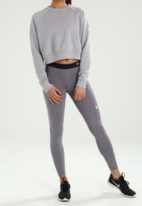 Grijze cropped sweatshirt met reliëfletters, gecombineerd met strakke grijze leggings met een subtiel patroon en zwarte sneakers.