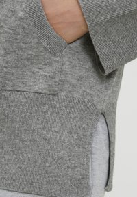 Pulover gri tricotat cu o textură ribbed, o deschidere laterală și un material moale. Prezintă un buzunar unghiular și un design lejer.