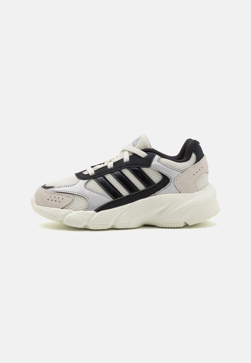Zapatilla deportiva gris y negra con materiales de malla y ante, que cuenta con tres franjas negras y una suela blanca gruesa con detalles texturizados.