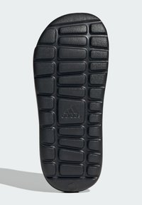 Semelle extérieure en caoutchouc noir avec un motif de grille texturé et le logo de la marque. Présente des rainures épaisses et rectangulaires pour une meilleure traction et durabilité.