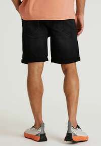 Zwarte spijkerbroekshorts met opgerolde manchetten en achterzakken. Draag met lichtgrijze sneakers met oranje zolen. Benen zichtbaar.