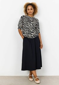 Sort og creme zebra-mønstret top med korte ærmer, parret med en svajende sort nederdel og nude sko. Minimalistisk design, afslappet stil.