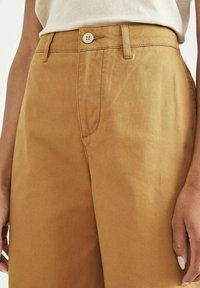 Ljusbruna bomullsshorts med en slät textur, som har en framficka, dragkedja och en enda knappstängning.