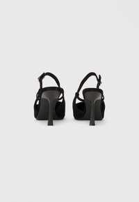 Fekete szarvasbőr magas sarkú szandál csattos pánttal, nyitott háttal és kúpos sarokkal, sima textúrával és minimalista dizájnnal.