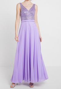 Pitkä laventelinsävyinen iltapuku, jossa paljetein koristeltu V-pääntie, laskeutuva hame ja istuva vyötärö. Puvussa on sileä ja ilmava rakenne.