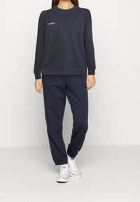 Felpa navy a maniche lunghe con polsini e orlo a costine, caratterizzata da un piccolo dettaglio testuale bianco. Abbinata a pantaloni jogging navy coordinati.