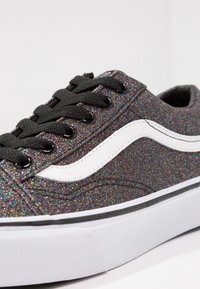 Baskets basses en tissu noir pailleté, bande latérale blanche, lacets noirs et semelle en caoutchouc blanche avec bordure noire.