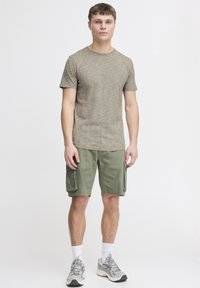 Olivengrønne cargo shorts med sidelommer, parret med en kortærmet, tekstureret, lysebrun t-shirt og grå løbesko.