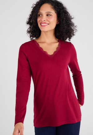 Haut à manches longues bourgogne avec un décolleté en V, doté d'une bordure en dentelle et d'une texture douce et lisse. Coupe décontractée avec un ourlet incurvé.