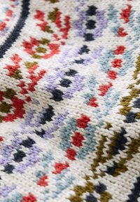 Tejido de punto en crema con intrincados patrones multicolores en rojo, azul, verde y morado. La textura es suave y tiene una apariencia acogedora.