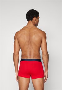 Boxer briefs vermelhos com uma ampla cintura azul marinho, apresentando uma textura suave e um design ajustado, vistos de trás.