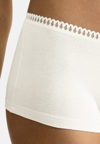 Hvide bomuldsshorts med en dekorativ blonderkant ved taljen. Stoffet er glat med et enkelt og minimalistisk design.