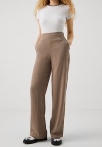 Beige high-waisted trousers with a wide-leg design, made from a lightweight material, featuring side pockets and a smooth texture.