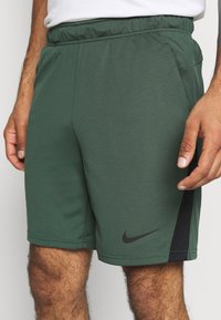Pantalones cortos deportivos verdes con cintura elástica, hechos de tejido transpirable. Presentan un logo negro de Nike y detalles laterales negros.