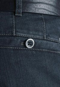 Un jean en denim noir présente un fermoir à bouton avec une finition en argent, des coutures contrastantes et un tissu texturé légèrement brillant.