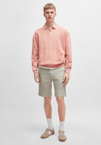 Felpa rosa chiaro con colletto e tasca anteriore, abbinata a pantaloni corti beige. Le scarpe sono sneaker marrone chiaro con accenti beige.