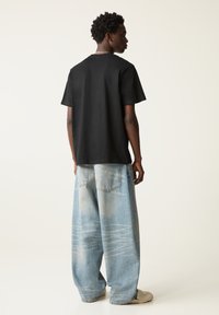 Sort t-shirt med korte ærmer, parret med lyseblå, vide jeans med falmede mønstre, og accessoriseret med en kraftig sølv halskæde.