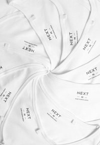 Valkoiset puuvillaiset hihattomat paidat aseteltuna spiraaliin, jossa on mustat painetut tarrat, joissa lukee "NEXT M MADE IN BANGLADESH", ja pehmeä rakenne.