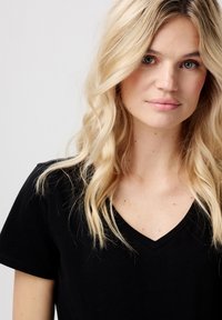 Sort V-hals t-shirt lavet af blødt stof, med korte ærmer og en klassisk pasform. Båret af en person med bølget blond hår.