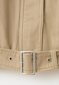Ceinture en tissu beige avec boucle rectangulaire en métal et coutures verticales sur un fond textile beige assorti.