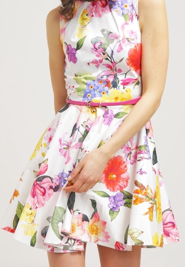 Robe florale avec un fond blanc, ornée de fleurs vibrantes de couleur rose, orange, jaune et violette. Elle a un corsage ajusté et une jupe évasée.