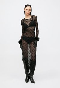 Čierne priesvitné šaty z priehľadnej sieťoviny s kvetinovým vzorom, vrstvené cez čiernu spodnú bielizeň. Dopĺňajú ich čierne rukavice a čierne čižmy až po kolená.