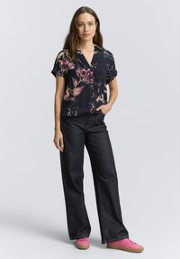 Blusa floreale navy a maniche corte abbinata a pantaloni larghi in denim scuro e scarpe da ginnastica rosa. Tessuto morbido con vivaci motivi floreali.