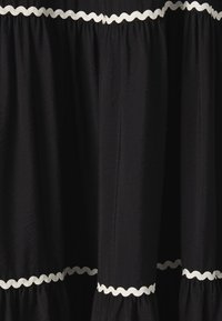 Robe noire avec un ourlet à volants et des bordures blanches en forme de vagues. Fabriquée en tissu doux, présentant des sections froncées et une silhouette fluide.