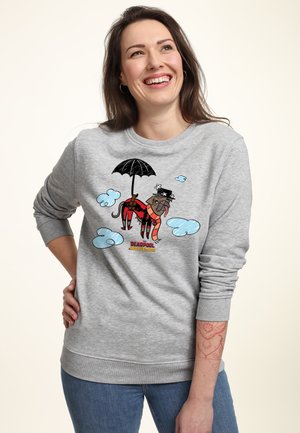 Smilende kvinde iført grå sweatshirt med tegneseriehund i rød superheltekostume, der holder en paraply, omgivet af blå skyer og teksten "Deadpool Wolverine".