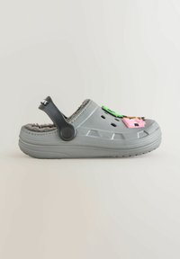 Sabot gris à enfiler avec intérieur duveteux, sangle arrière noire réglable et breloques décoratives colorées sur le dessus. Comprend des trous de ventilation.