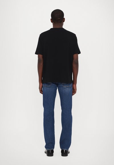 T-shirt noir à manches courtes associé à un jean en denim bleu, avec une coupe droite et un design épuré et minimaliste.