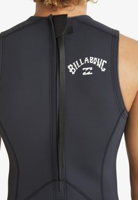 Traje de neopreno negro con un cuello alto, fabricado en material de neopreno liso y con cierre de cremallera en la parte posterior. Logo de "Billabong" impreso en blanco.