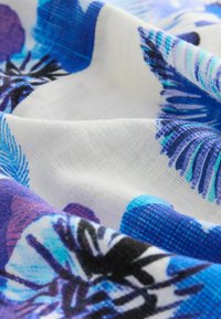 Vitt tyg med blå och lila blommönster; lätt, slät textur, vikt för att visa detaljer och färgkontrast.