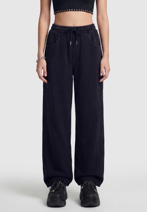 Person iført sorte vidde cargo bukser med snøre i taljen, sort crop top, chunky sorte sneakers med kæder og et sølvarmbånd.
