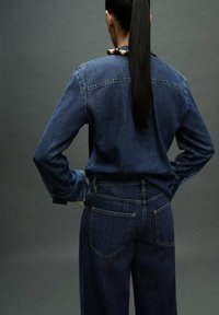 Denim shirt and high-waisted jeans in dark blue. Features include button-down collar, long sleeves, and two back pockets.