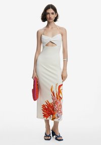 Halter neck dress with ribbed white bodice, cream skirt featuring coral and sea life print, paired with a textured pink handbag and blue heels.