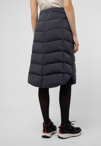 Jupe en velours côtelé gris foncé, avec un motif matelassé, longueur genou et fente à l'arrière. Associée à des baskets noires et des collants noirs.