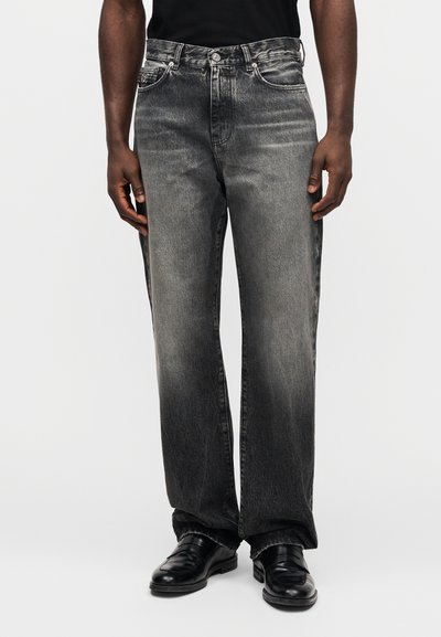 Pilki džinsai iš džinso medžiagos, laisvo silueto, su išblukusiais lopais, penkių kišenių dizainu ir metalinėmis detalėmis. Dėvimi su juodais batais.