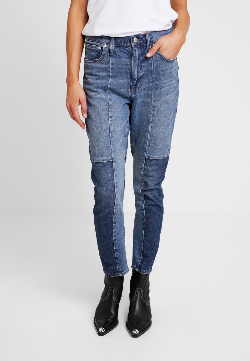 Jeans de mezclilla de parches en azul claro y oscuro, con un ajuste slim, que cuentan con bolsillos y cierre de botón, combinados con botas de tobillo puntiagudas negras.