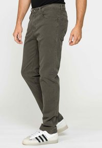 Chino in cotone khaki con una trama liscia, vestibilità slim, design a cinque tasche e cuciture sottili; abbinati a sneaker bianche con strisce nere.