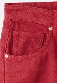 Gros plan sur la poche d'un jean en denim rouge avec des coutures visibles et deux rivets argentés aux bords supérieur et inférieur.