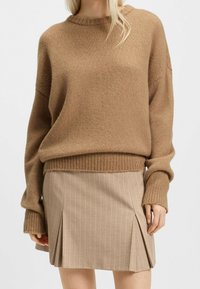 Pull marron tricoté avec un ourlet et des poignets côtelés, associé à une jupe beige à fines rayures avec des plis et une coupe droite.