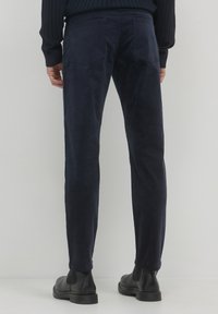 Pantalons en velours côtelé bleu marine à coupe droite, dotés de poches arrière et d'une texture douce, associés à des bottines noires.