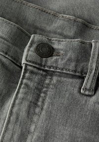 Jean en denim gris avec un bouton en métal noir portant l'inscription "TWO SOON JEANS", présentant des coutures visibles et une surface douce et texturée.