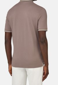 Polo tričko ze světle hnědé látky s krátkými rukávy, kontrastní bílý límec a akcenty na rukávech, hladká textura a boční rozparek.