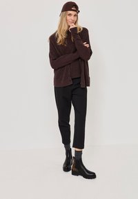 Tmavě burgundský kardigan s volným střihem, černé kalhoty a černé boty s leopardím potiskem. Modelka nosí odpovídající čepici.