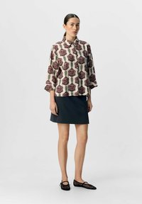 Blusenshirt mit Blumenmuster in Creme mit lila Rosen und grünen Akzenten, kombiniert mit einem dunkelgrauen Rock und schwarzen Ballettschuhen aus Netz.