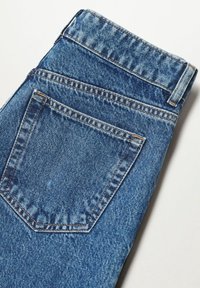 Jeans de denim azul, con un bolsillo trasero con costuras en ángulo, un acabado texturizado y una apariencia ligeramente desgastada.