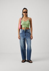 Zöld, testhezálló, ráncolt crop top, megkötő részlettel, világoskék, széles lábú farmernadrággal és fekete szandállal párosítva. Rózsaszín kézitáska kiegészítőként.