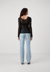 Svart, langermet topp med teksturert mønster og bred bakhals, parret med lyseblå, vide jeans.